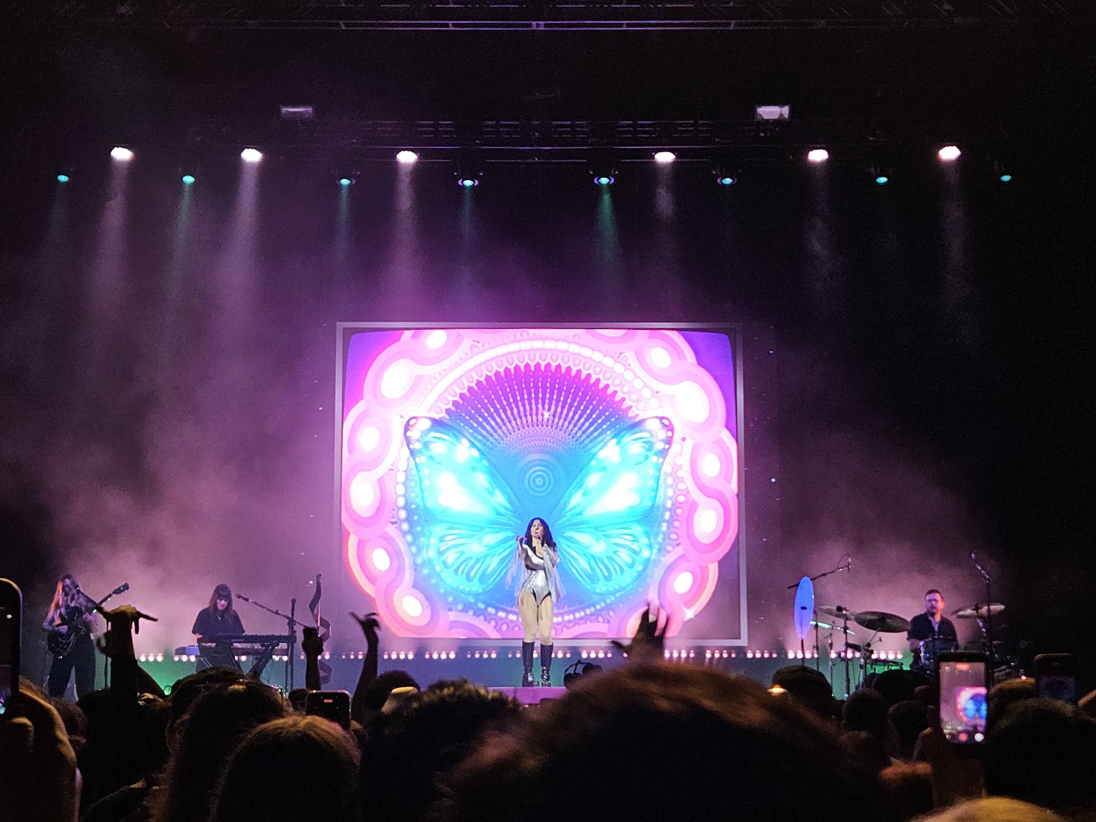 Marina on stage with a large image of a butterfly behind her.